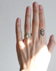 Hand wearing a ring with a green gemstone on a plain background