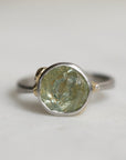 Ring with a green gemstone and platinum band with yellow gold details on a light gray background