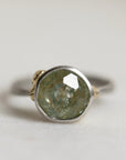 Ring with a green gemstone and platinum band with yellow gold details on a light gray background