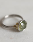 Ring with a green gemstone and platinum band with yellow gold details on a light gray background