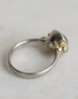 Ring with a green gemstone and platinum band with yellow gold and diamond details on a light gray background
