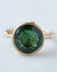 round green faceted tourmaline stone in a gold bezel ring with gold barnacles. Front view.