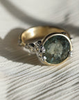 Gold ring with a green gemstone and barnacles on a light background