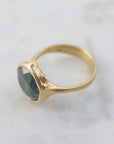 steely blue color change sapphire set in a gold bezel and band. Around the cup of the bezel are tiny gold barnacles. Photographed front side and in natural light.