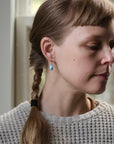 Woman with braided hair wearing a gray sweater and blue earrings.