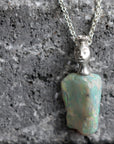 Necklace with an opal pendant featuring a face on a textured gray surface