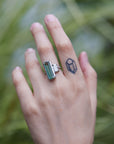 long, rectangular tourmaline stone set with prongs next to a diamond baguette. The ring is platinum, and shown on hand.