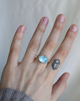 hand wearing blue gemstone ring against a pale background