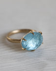 Gold ring with a blue gemstone on a light gray background