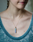 Person wearing a necklace with a blue pendant, blurred background