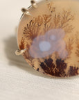Oval agate stone with tree pattern on a white fabric background