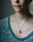 Person wearing a necklace with a pendant against a neutral background