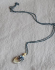 Necklace with a clambshell fossil pendant on a textured fabric background