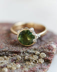 A 2.74ct tourmaline ring. The tourmaline is a deep green and is set in 14k gold with a 14k gold band. The rsetting is encrusted with bright sterling silver barnacles. The ring is viewed from the front and sits on a stone.