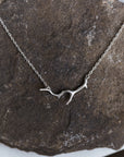 A bright sterling silver necklace with a silver coral shaped pendant. The necklace is draped on a stone.
