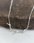 A bright sterling silver necklace with a silver coral shaped pendant. The necklace is draped on a stone.