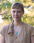 Woman with a braid and turquoise necklace and earrings standing in front of green foliage
