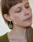 green teardrops under silver scallop ear wires. Photographed on person.