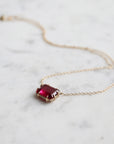 pink rectangular stone with in gold prongs on a gold chain with diamonds set in a hidden halo on the side of the setting. photographed on white marble.
