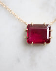 pink rectangular stone with in gold prongs on a gold chain with diamonds set in a hidden halo on the side of the setting. photographed on white marble.