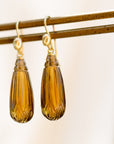 carved brown quarttz drops hang beneath gold ear wires with faces
