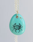 Turquoise pendant with crab design on a light gray background