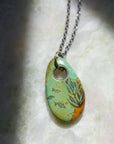 Necklace with a turquoise pendant featuring fish and seaweed illustrations on a textured surface