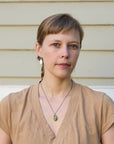 Woman with a braid wearing a beige top and necklace against a neutral background
