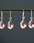 two pairs, silver and gold, pink pearl earrings with rose flower ear wires hang from a brass bar.