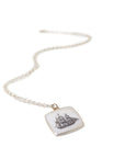 a square mother of pearl slice is set in silver with a gold ring and silver chain. An old whaling ship is hand etched into the surface with black ink, called scrimshaw.