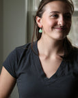 woman wearing dark grey shirt with bright green earrings