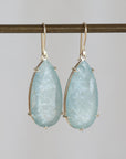 Teardrop-shaped earrings with light blue gemstones on a gray background