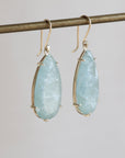 Teardrop-shaped light blue gemstone earrings on a gray background
