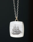 a square mother of pearl slice is set in silver with a gold ring and silver chain. An old whaling ship is hand etched into the surface with black ink, called scrimshaw.