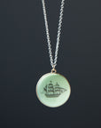 melon green round variscite cabochon is set in a gold bezel and hangs beneath a silver chain. an old whaling ship is hand-etched into the surface with black ink.