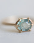 14k yellow gold ring with a light blue Montana sapphire on a soft white fabric background.