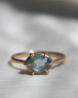 14k yellow gold ring with a light blue Montana sapphire on a soft white fabric background.