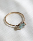 Side view of 14k yellow gold ring with a light blue Montana sapphire and a halo of small diamonds around the setting on a soft white fabric background.