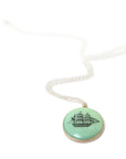 melon green round variscite cabochon is set in a gold bezel and hangs beneath a silver chain. an old whaling ship is hand-etched into the surface with black ink.