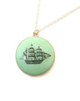 melon green round variscite cabochon is set in a gold bezel and hangs beneath a silver chain. an old whaling ship is hand-etched into the surface with black ink.