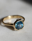 Gold ring with a blue gemstone on a light gray background