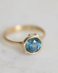 Gold ring with a blue gemstone on a light gray background