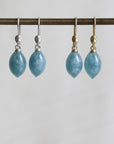two pairs of blue teardrop earrings on a metal rod against a white background