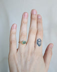 Hand wearing a gold ring with a green gemstone on a plain background