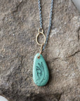 green turquoise teardrop bead with gold link and black chain. a scrimshaw hand is inked to the surface.