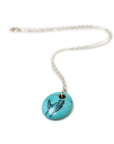 kingman turquoise bead pendant necklace on silver chain with gold bail. A scrimshaw hand is inked to the front.