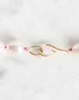 A close-up of a pearl necklace with a gold clasp on a light marble surface. The necklace features large, irregular white pearls separated by small pink accents, with a polished gold S-shaped clasp.