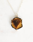 A silver necklace with a hexagonal pendant featuring a polished tiger's eye stone, displayed on a clean white background.