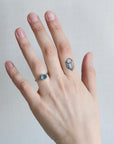 Hand wearing a ring with a blue gemstone on a neutral background