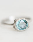 A silver ring featuring an oval-cut light blue gemstone, photographed on a clean, light gray background.